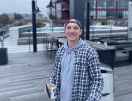 A man wearing a plaid jacket and backward baseball cap smiles.
