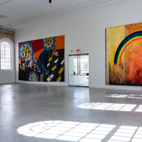 A colorful quilt and painting of a rainbow in a large installation space.