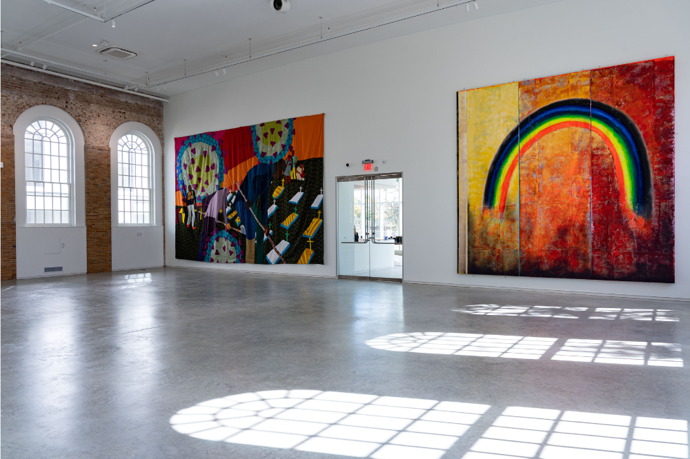 A colorful quilt and painting of a rainbow in a large installation space.