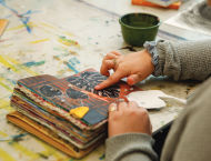 Hands hold open a colorful, artsy journal.