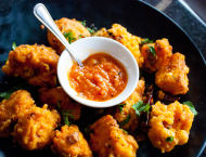 Fried food with herbs and peppers sit on a plate with sauce.