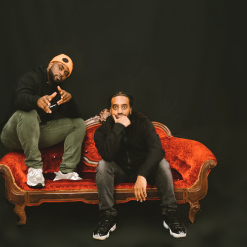 Two men sit on a red couch in a black room.