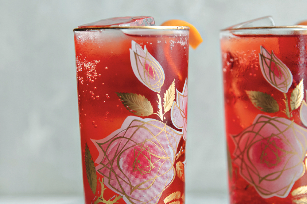 Two drink glasses with rose decorations on the outside of the glass and red liquid inside.