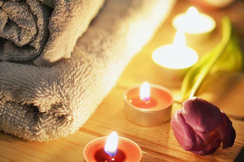 Lit candles sit next to bath towels and a red tulip.