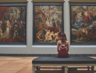 A person sits on a bench, looking at paintings in a museum.