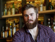A man in a purple shirt stands in front of a bar.