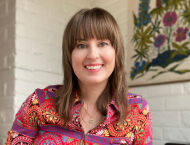 A woman with bangs in a patterned red top smiles at the camera.