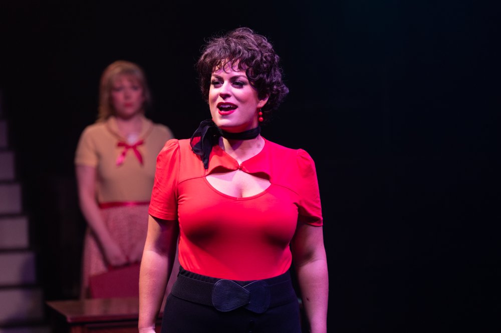 A woman in a red shirt sings on stage.