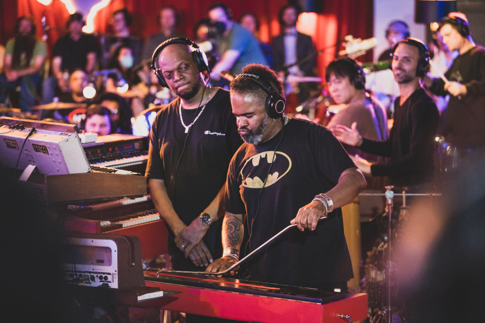People in Batman t-shirts stand next to a keyboard.