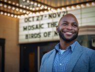 A man in a blue shirt looks to the right in front of Mosaic Theater.