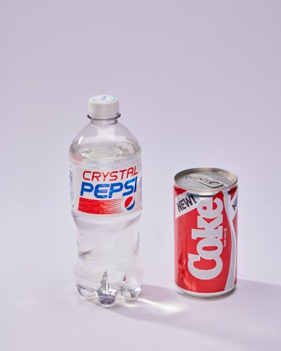 A clear bottle of Pepsi sits next to a small can of Coke.